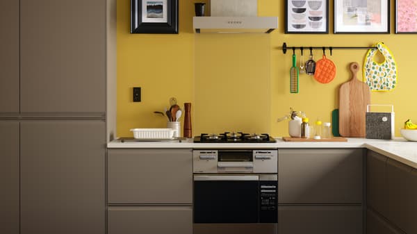 A matt dark beige kitchen with a white marble effect worktop, plus black rails and pictures in black frames on a yellow wall.