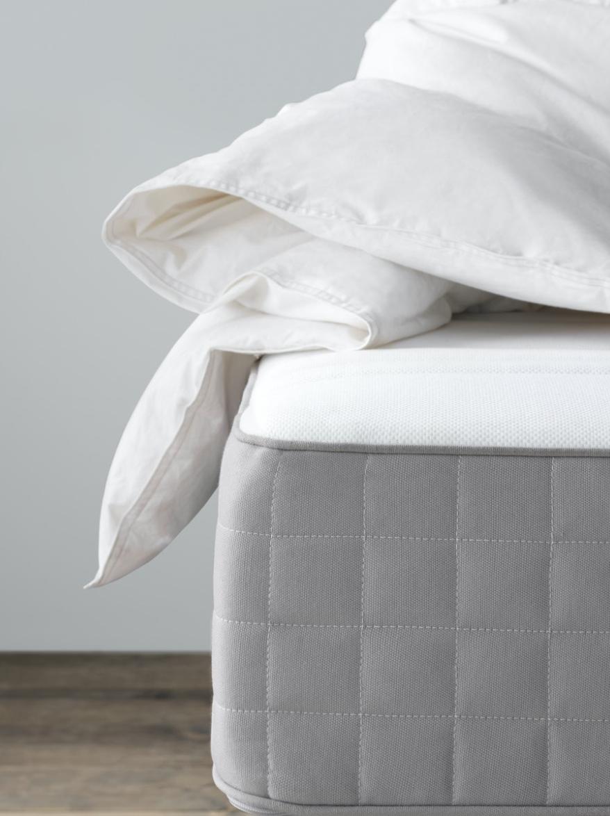 A mattress corner with white blanket shown on top of it.