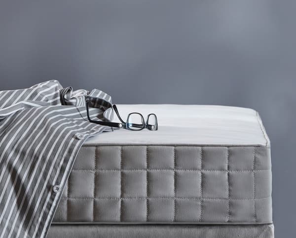 A mattress with grey edge and shirt and glasses on top.