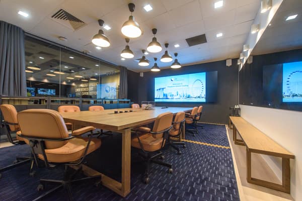 A meeting area with a long wooden table and swivel chairs placed on top of a dark blue carpet. 