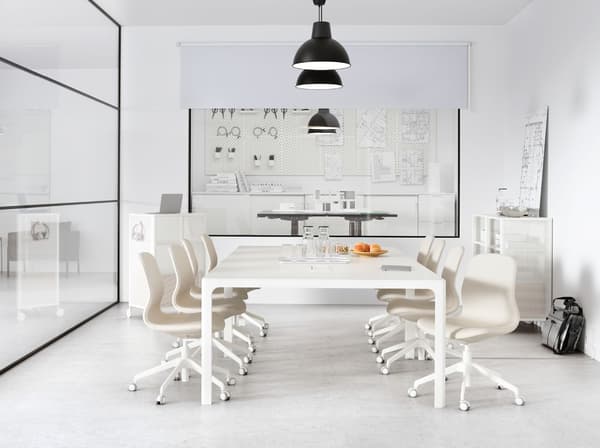 A meeting room with a glass wall containing a large white table. A row of black SKURUP pendant lamps hang from the ceiling.