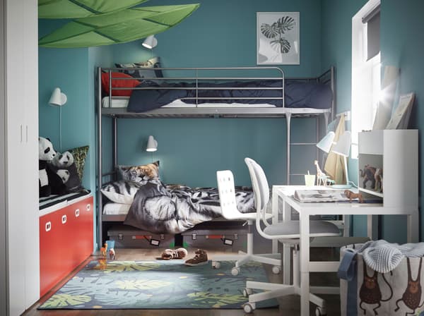 A metal bunk bed frame with animal printed textiles and a white desk, against a blue-green wall.