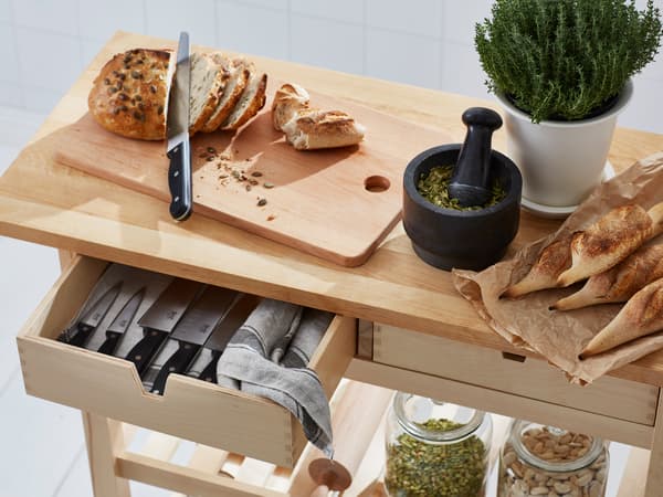 A metal kitchen island on wheels stocked with jarred ingredients sits next to a kitchen counter.