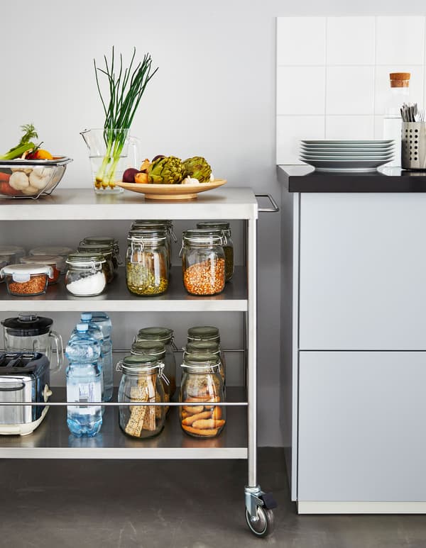 A metal kitchen island on wheels stocked with jarred ingredients sits next to a kitchen counter.