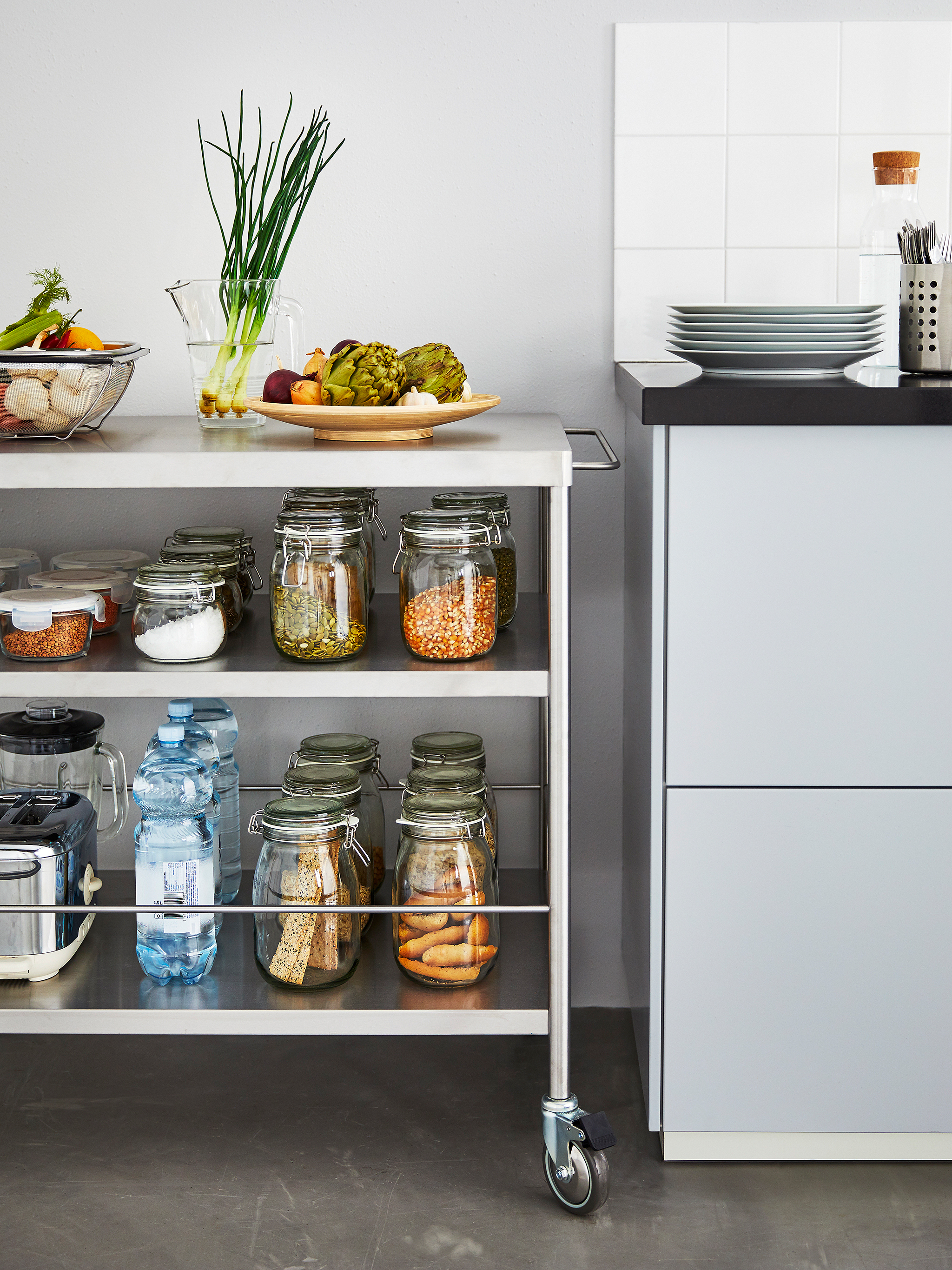 A metal kitchen island on wheels stocked with jarred ingredients sits next to a kitchen counter.