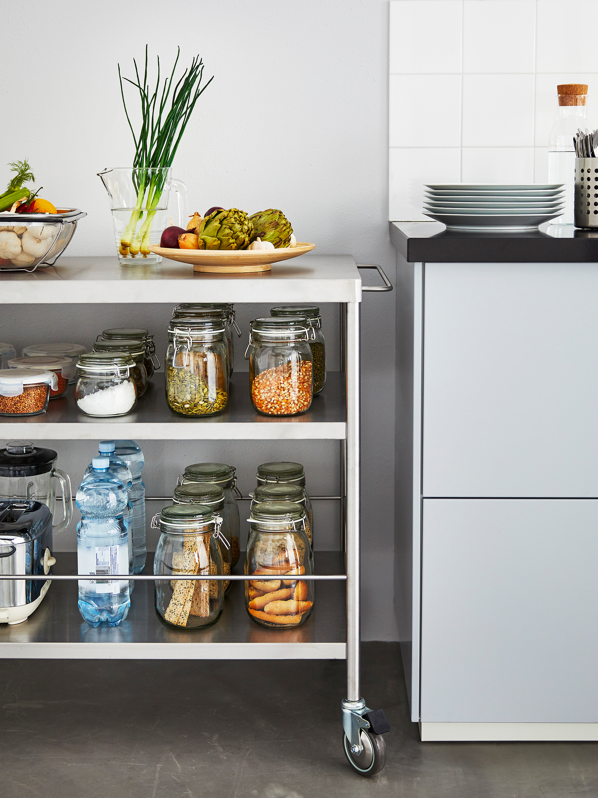 A metal kitchen island stands next to a kitchen counter storing several glass jars with dry goods and vegetables.