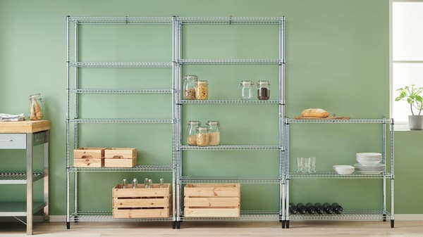  A metal shelf with glass jars, wooden crates, plates, and wine bottles stands against a green wall.