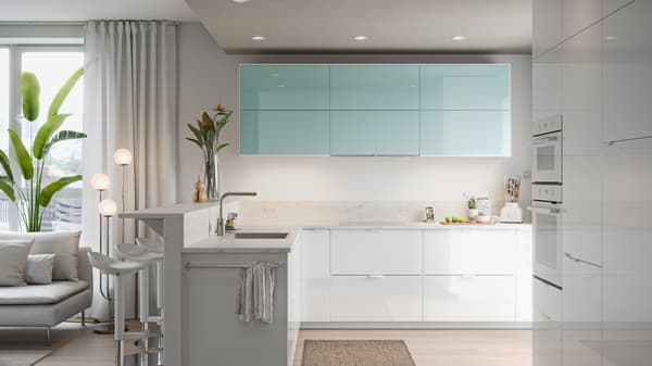 A METOD kitchen in white with a sink, a sofa, and on the wall are cabinets with JÄRSTA kitchen fronts in light turquoise.