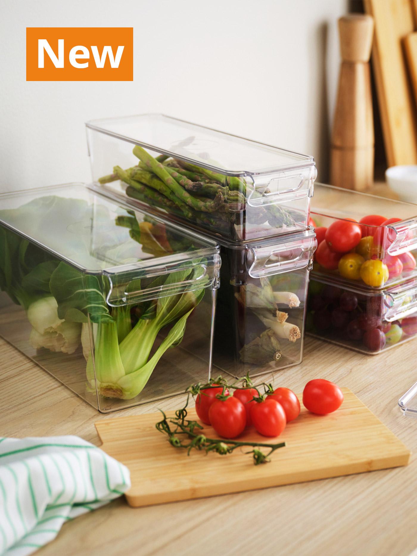 A mid shot of a transparent set of 6 KLIPPKAKTUS storage box for the fridge on the kitchen counter being used to organise fresh vegetables. Overlaying the image, orange tag that reads 'New' on the top left corner.