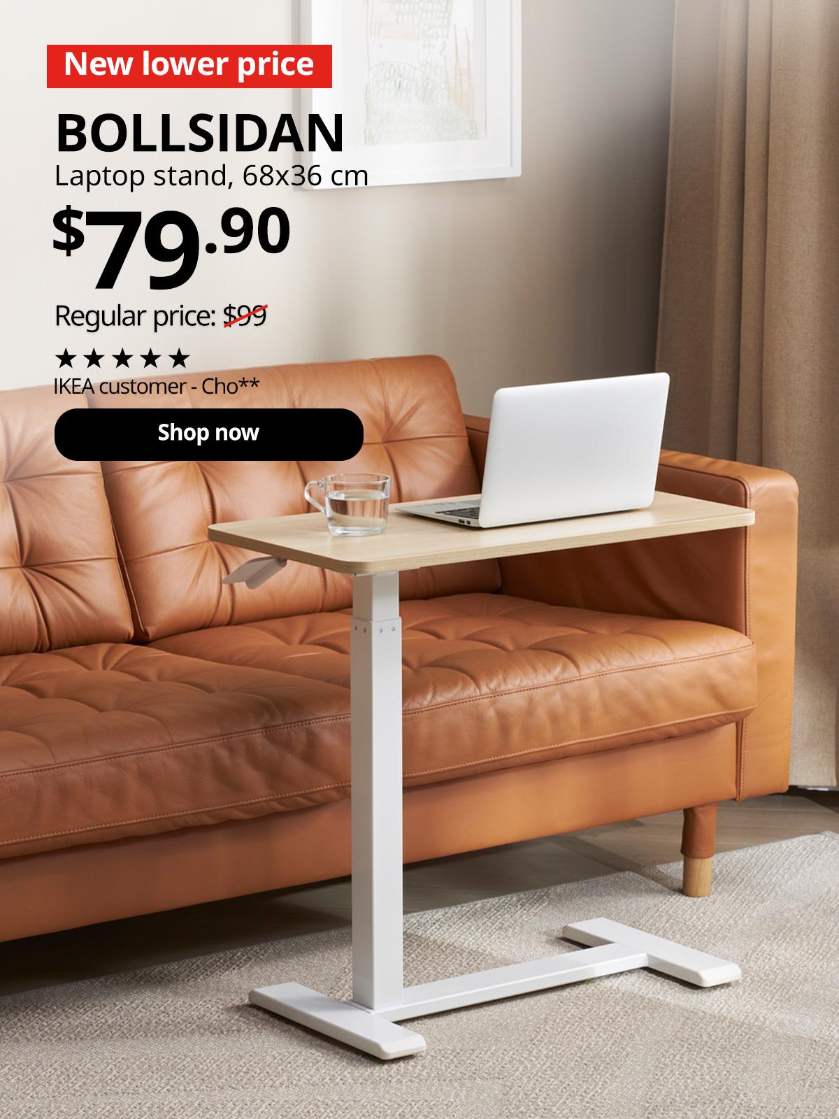 A mid shot of a white stained oak effect/white BOLLSIDAN laptop stand placed next to a Grann/Bomstad Golden-Brown LANDSKRONA 2-seater sofa in a living room setting . In the top left corner, a red tag with white text reads 'New lower price'. Accompanying white text displays: 'BOLLSIDAN, Laptop stand, 68x36 cm, $79.90, Regular price: $99'
