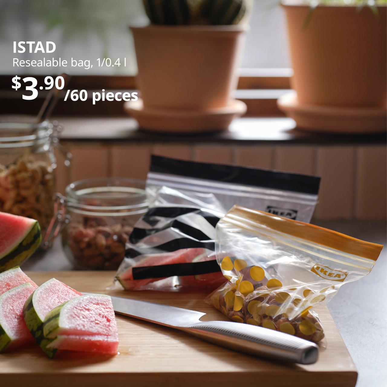 A mid shot of patterned black and patterned yellow ISTAD resealable bag used to pack watermelon and nuts on a wooden chopping board. On the top left corner, white text overlay image that reads "ISTAD, Resealable bag, 1/0.4 l, $3.90/60 pieces".