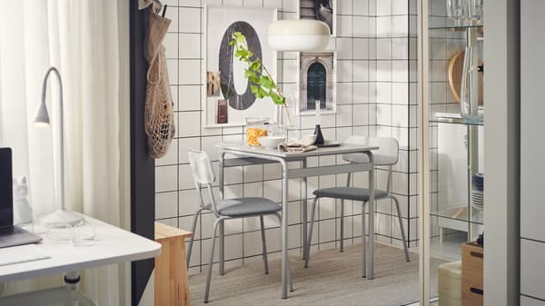 A minimal, industrial-style studio with a dining area consisting of a grey GRÅSALA table and two chairs beside a tiled wall.