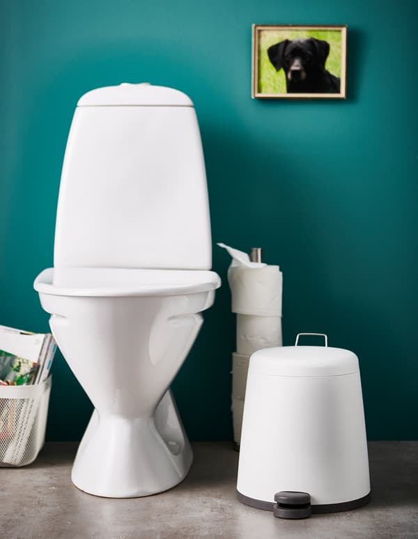 A minimalist, white waste bin sits next to a toilet seat in a bathroom.