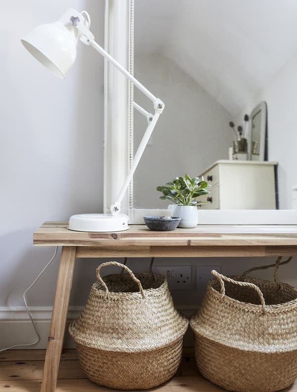 A mirror and lamp on top of a wooden bench with two storage baskets underneath.