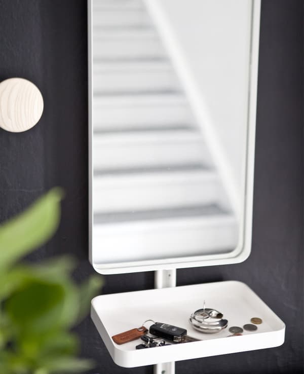 A mirror and small white tray containing keys and coins against a black wall.