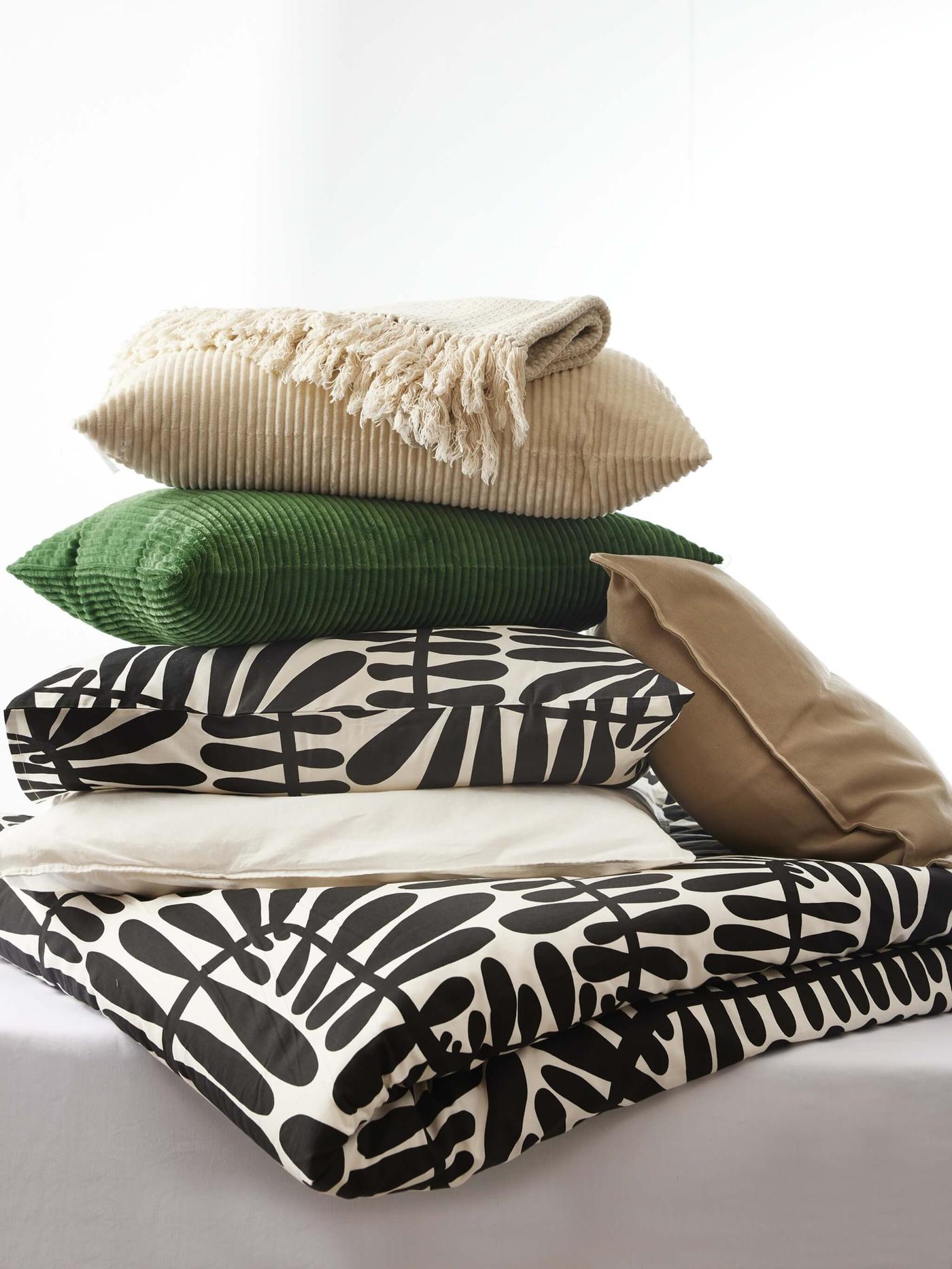 A mixture of bed textiles stacked on top of each other with brown, black and white colors in front of a white background.