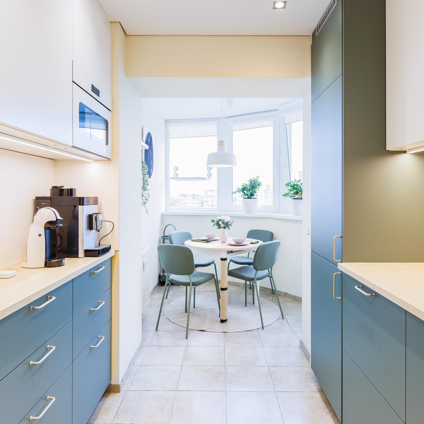 A modern corner kitchen with grey-green and white fronts, leading into a cosy dining area with a round table and green chairs.