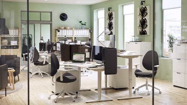 A modern furnished office environment with light green walls and white BEKANT adjustable corner desks and chairs.