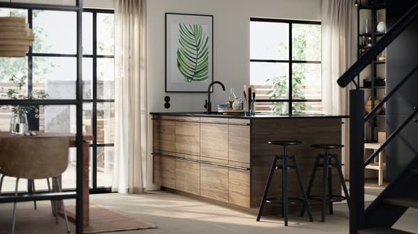 A modern kitchen with a central island featuring STENSTA fronts in dark brown stained ash veneer and black stools.