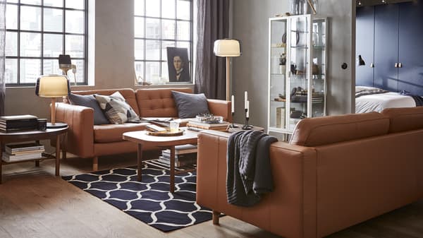 A modern living room with a glass storage cabinet, brown leather sofas and round dark wooden coffee tables.