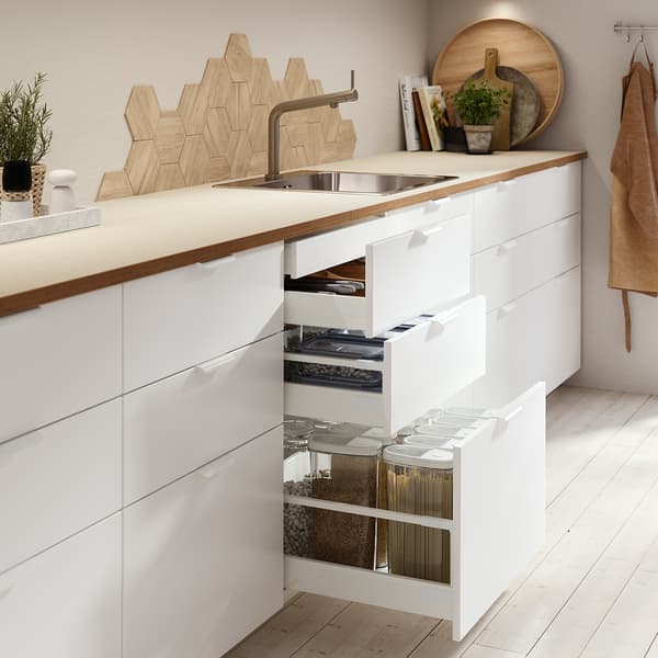 A modern white kitchen with an oak worktop, featuring open drawers with drawer organisers and containers. 