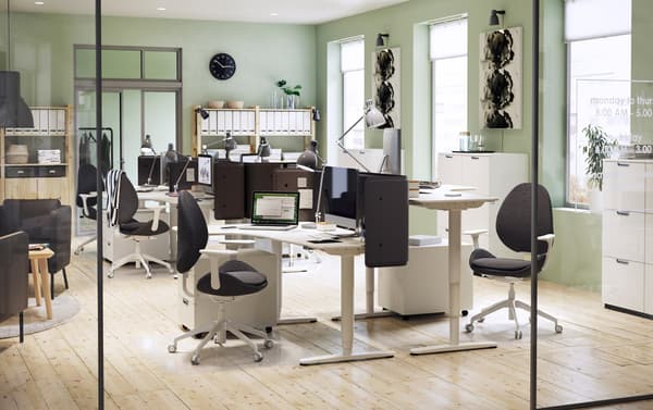 A modernly furnished office environment with light green walls and white IKEA BEKANT adjustable corner desks.