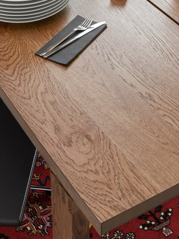 A MÖRBYLÅNGA dining table on a red Persian rug. On the table are a stack of plates, a black napkin and a knife and fork.