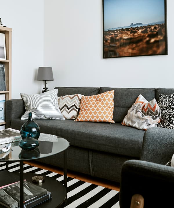 A monochrome living room with gray sofa, black and white striped rug, a round black and glass coffee table.