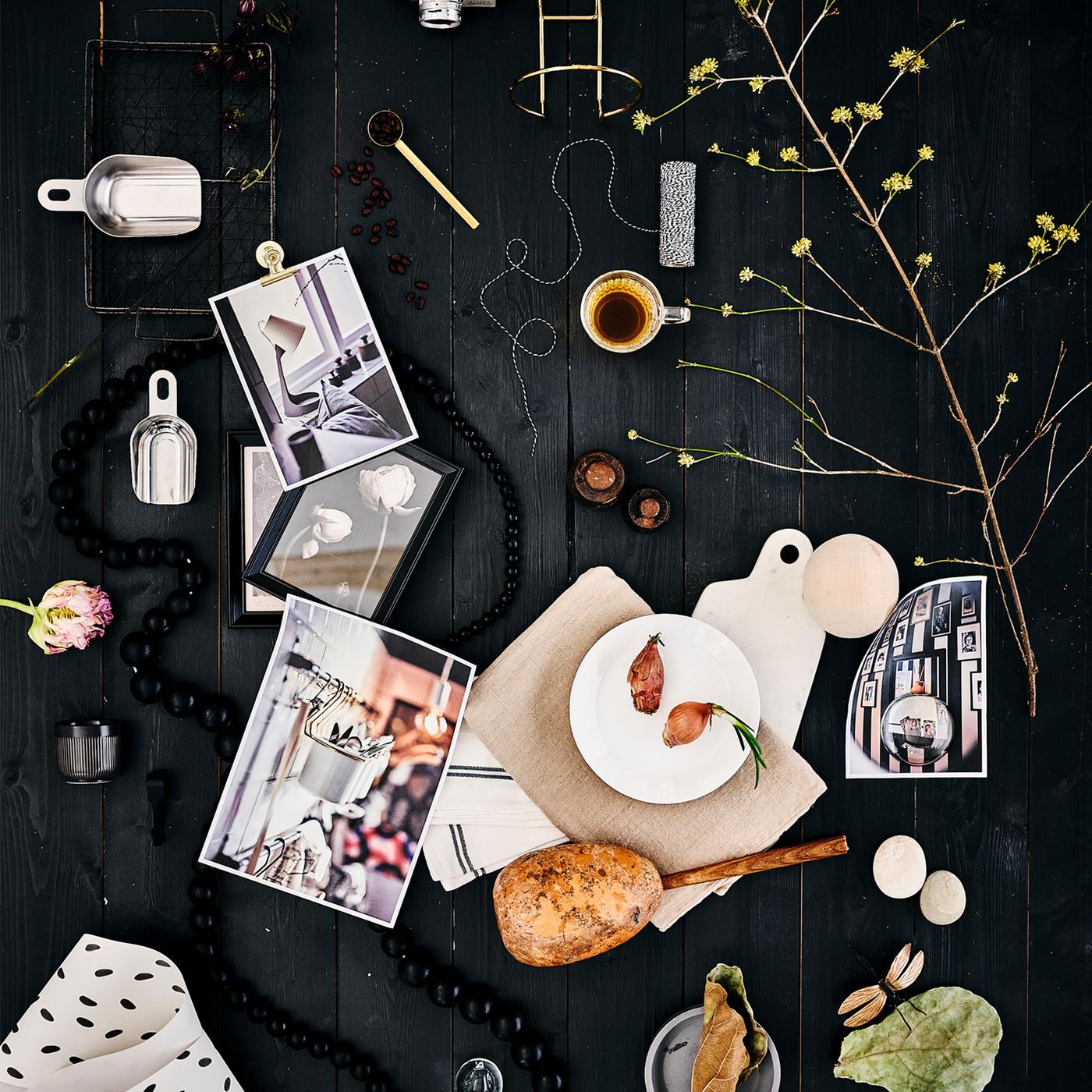 A mood board on a black wood background with a white OFTAST plate, white textile with black flecks, an espresso and leaves.