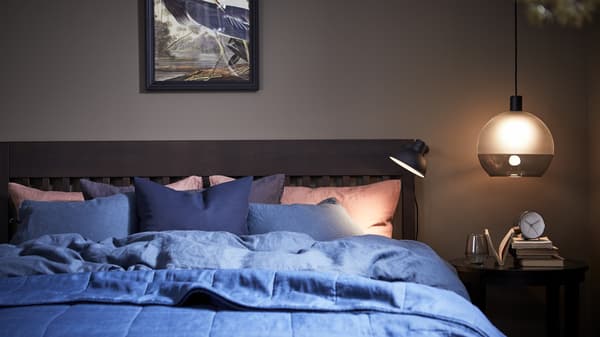 A moodily-lit bedroom with an IDANÄS bed frame with a PUDERVIVA quilt cover and pillowcases in dark blue.