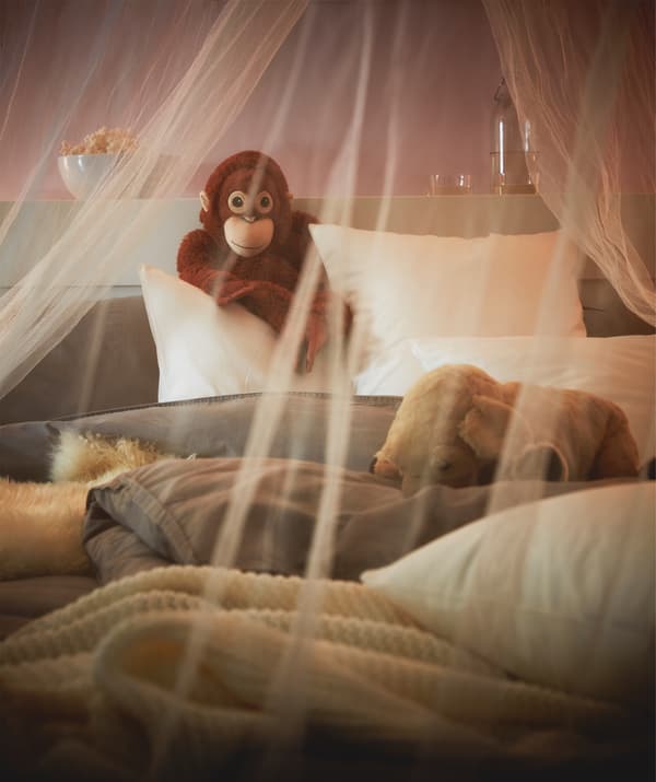 A mosquito net draped over a fluffy, unmade bed, and a toy monkey propped up against the headboard.
