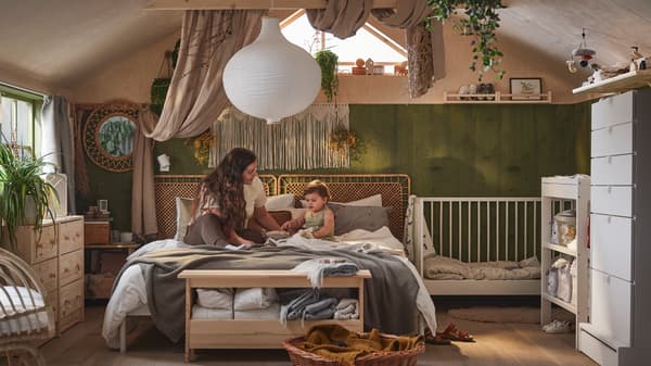 A mother and child interacting on a VEVELSTAD bed that’s covered in neutral-coloured textiles beside a white GULLIVER crib.