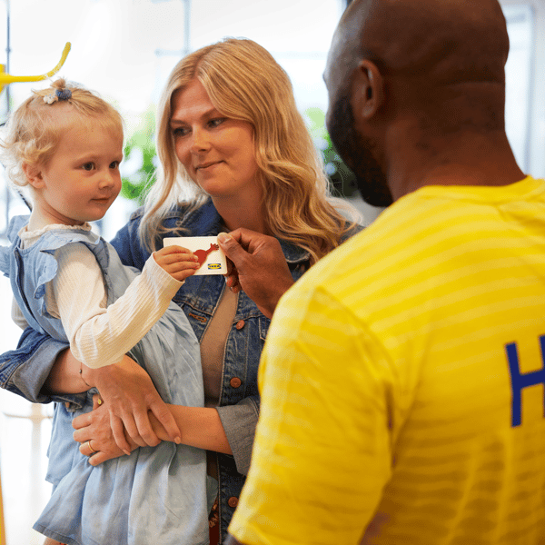 A mother and child receiving an IKEA refund card from an IKEA worker.