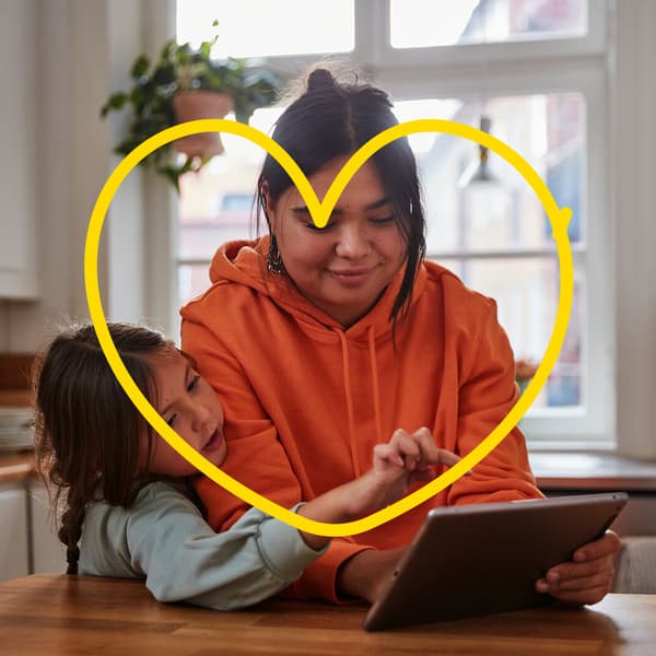 A mother and her daughter at home at the dining table with a tray, above it an IKEA illustration of a heart.