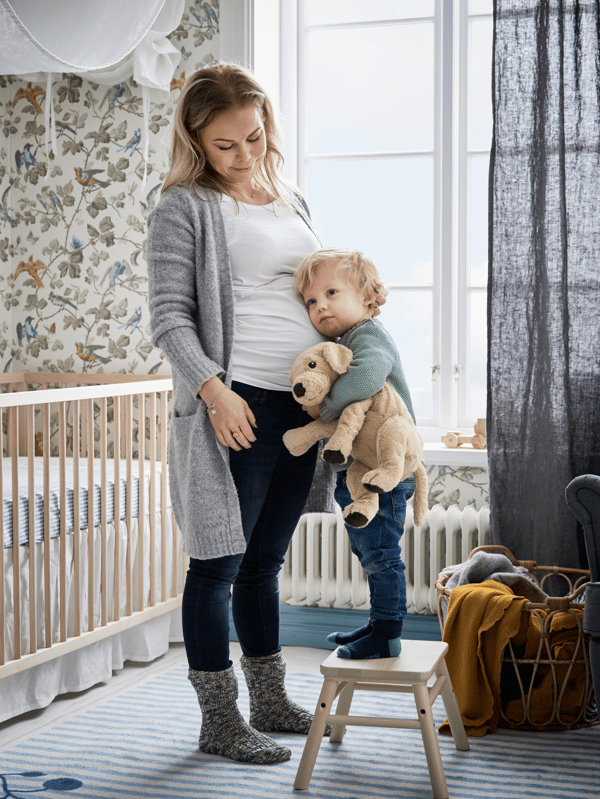 A mother and toddler standing in a cozy room with a soft toy, labeled “Gifts for mom”