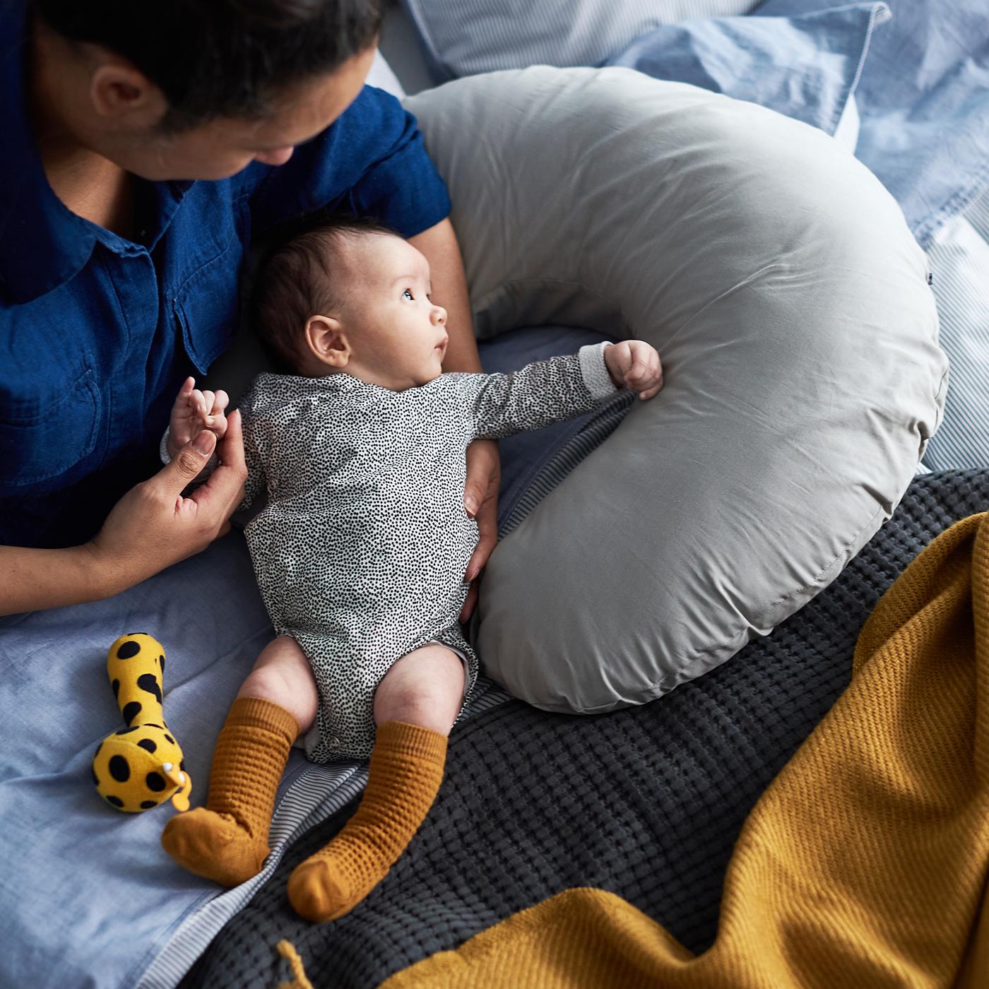 A mother holding a baby with a speckled romper in her lap, with a yellow/black KLAPPA rattle next to the baby.
