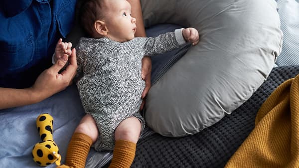 A mother holding a baby with a speckled romper in her lap, with a yellow/black KLAPPA rattle next to the baby.