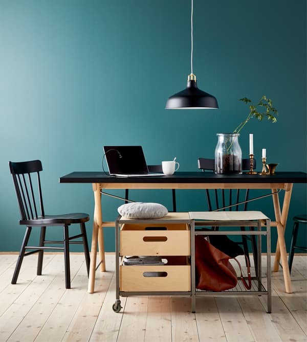A movable storage bench with castors next to a large dining table that’s being used as a study or work space. 
