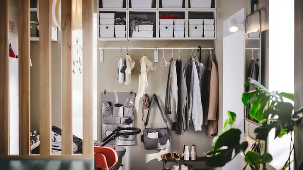A MULIG clothes bar on a hallway wall holding outdoor clothes, with a LEN hanging storage and hooks on the wall below it.