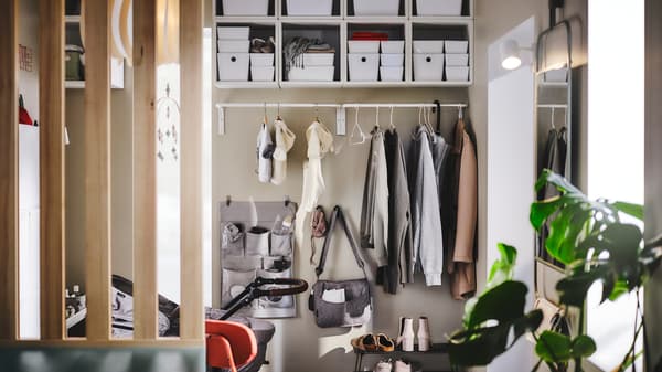 A MULIG clothes bar on a hallway wall holding outdoor clothes, with a LEN hanging storage and hooks on the wall below it.