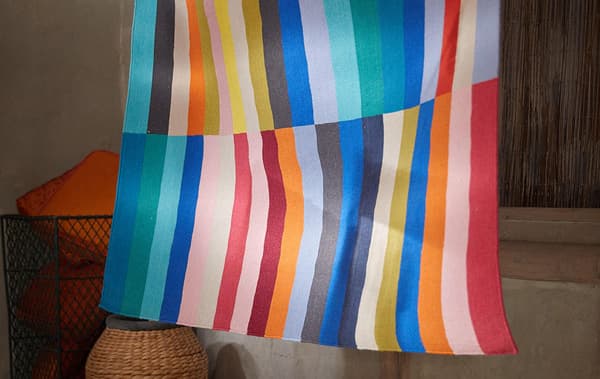 A multi-color striped pattern hanging in a shaded room with neutral surroundings.