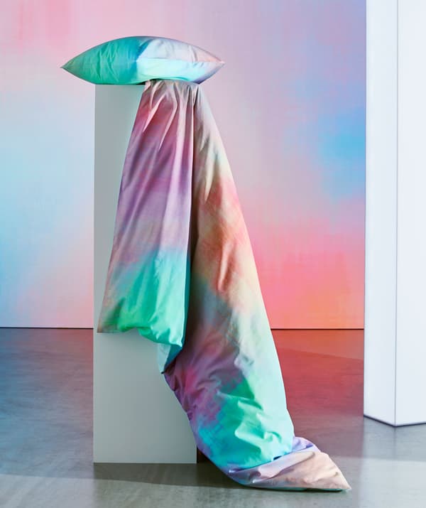 A multicolor pillow and quilt positioned on a pedestal.