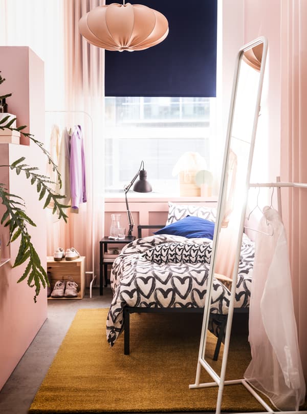 A narrow room in a rosy colour scheme with a GRIMSBU bed, a tall KNAPPER mirror and ample room to store and display clothes.