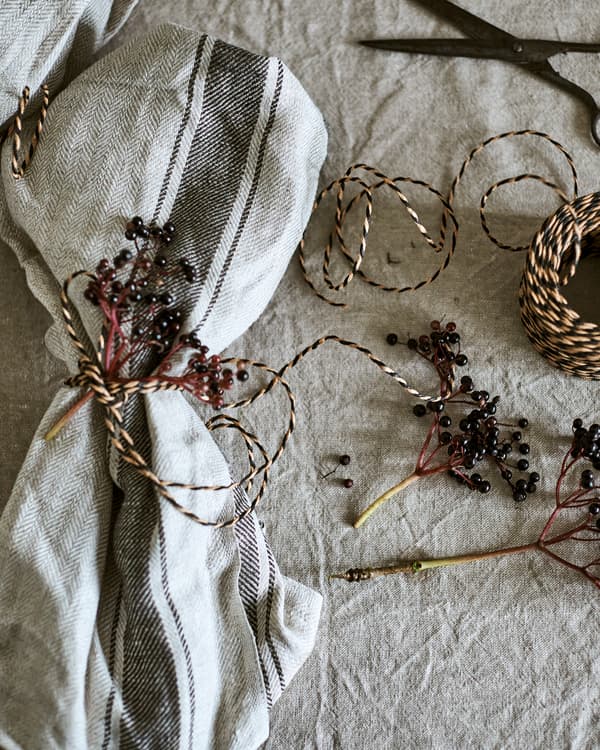A natural coloured tea towel used as a napkin and decorated with twine and wild berries. A ball of twine is at the side.