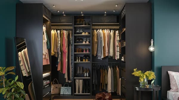A neat dark-brown PAX wardrobe with clothes in it and light illuminating the inside of it.