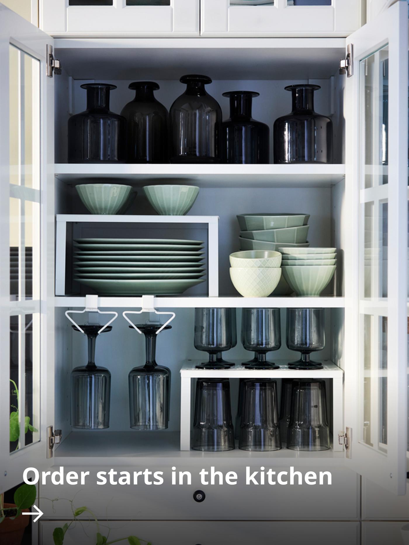 A neatly arranged kitchen wall cabinet fitted with PÅLYCKE organisers containing tableware and drinking glasses.
