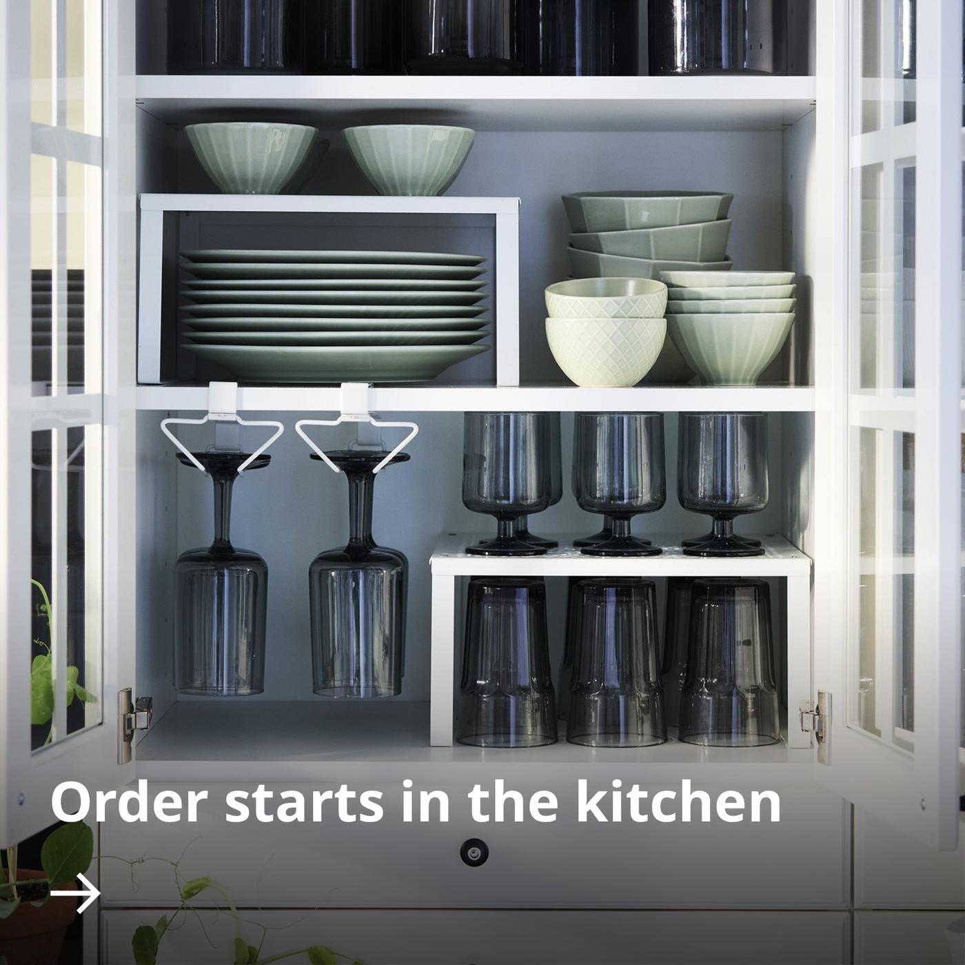 A neatly arranged kitchen wall cabinet fitted with PÅLYCKE organisers containing tableware and drinking glasses.