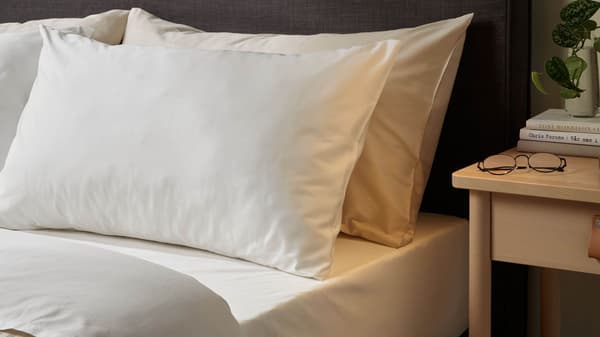 A neatly made bed with pillows and a dark gray upholstered headboard next to a birch nightstand with a lamp on it
