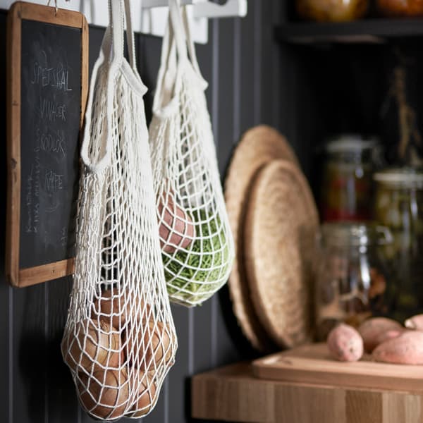 A net bag hanged up on a black wall. The bags are filled with vegetables.