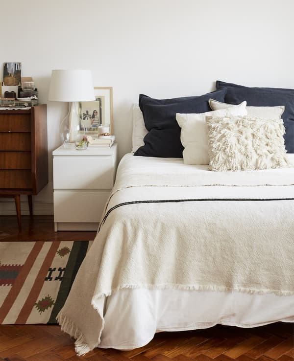 A neutral coloured bedroom, with a small white bedside table with lamp.